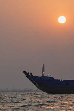 The sun sets over commercial vessels anchored in the Strait of Hormuz off Bandar Abbas, Iran, with the city's skyline in the background, on Sunday, Sept. 6, 2026.