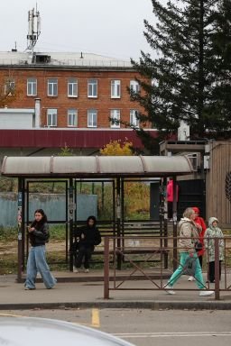 People are seen at a bus stop in Shelekhov, a Russian town near the city of Irkutsk, on Thursday, backdropped by the district hospital and the medical center for treating infectious diseases.