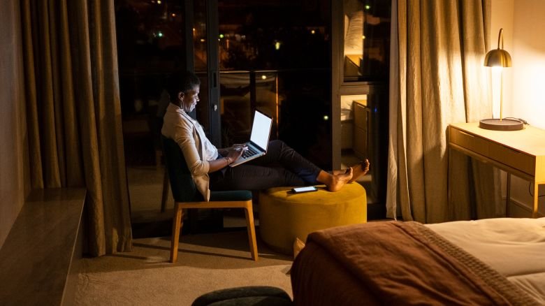 Wide shot of African female using laptop in hotel room at night