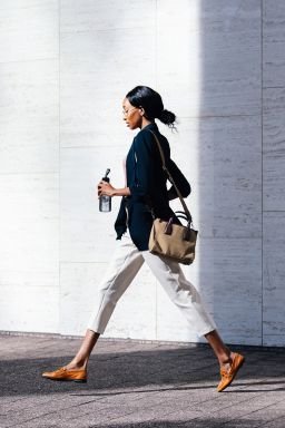 Confident black businesswoman walking in the city carrying a bag and a water bottle, showcasing modern urban lifestyle.